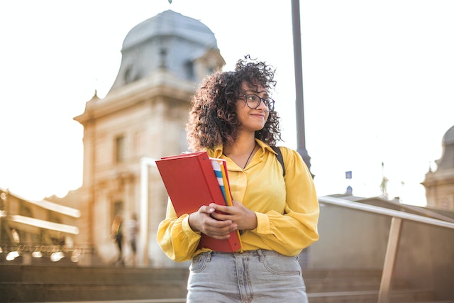 A female student standing still and smiling while holding a pen and a notebook, presumably contemplating IB IA topic suggestions.