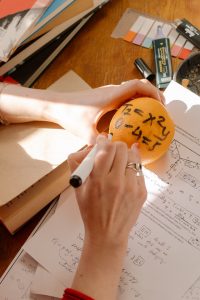 A student creatively illustrates mathematical numbers on a fresh orange during an IB Math Studies class at school.
